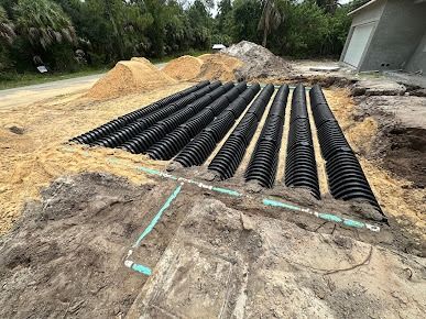 Septic system installation: black corrugated pipes in trenches, surrounded by dirt and sand.