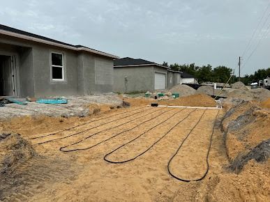 Underground irrigation system installation in sandy soil near new houses. Black tubing laid in trenches.