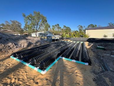 Black septic system pipes installed in sandy soil with blue sky.