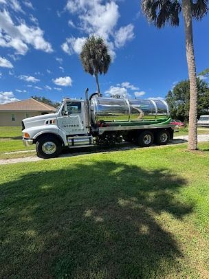 White septic tank truck parked on green grass, under blue sky with clouds.