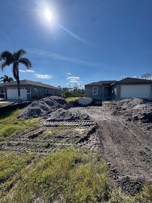 Construction site with two new houses, piles of gravel, and blue sky.