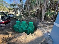 Green septic tanks in a hole, being installed near a building and excavator.