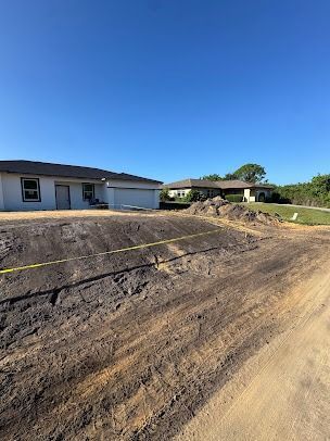 Dirt road in front of houses; construction site with dirt pile, caution tape. Clear, blue sky.