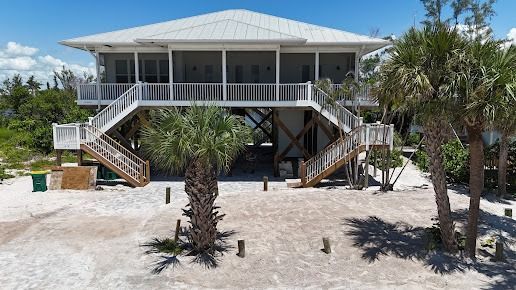 Beach house on stilts with white exterior, stairs, and palm trees.