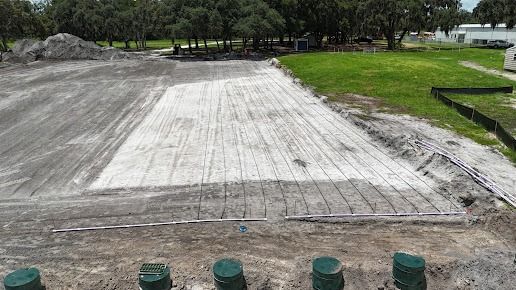 An open plot of land with rows of white material, possibly sand, surrounded by dirt and grass.