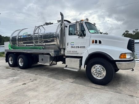 White septic truck parked outdoors on a gray surface, with silver tank and green hoses.