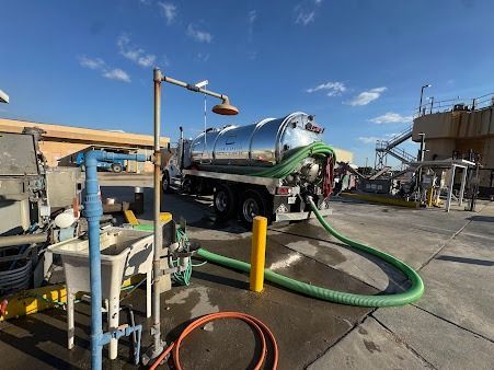 A vacuum truck with a green hose, parked at a facility on a sunny day.