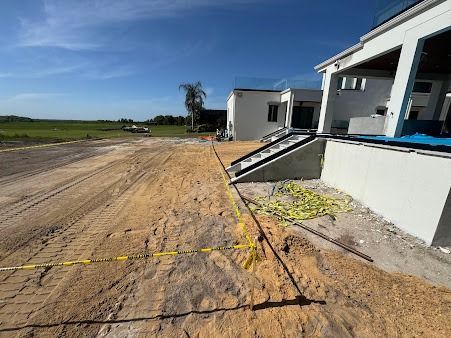 Construction site with dirt path leading to a white building; caution tape, and equipment visible.