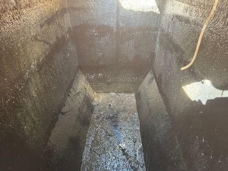 Inside view of a dark, narrow, concrete structure with wet surfaces. A light-colored cord hangs from the upper right.