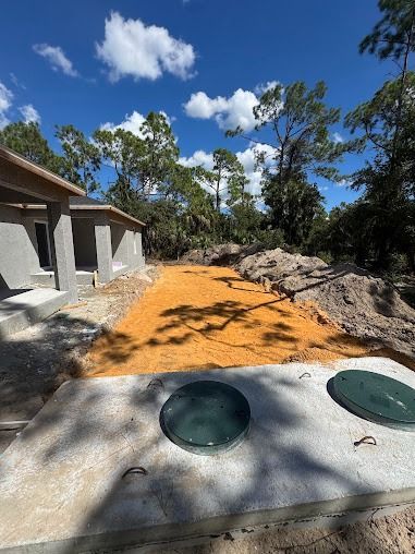 Septic tanks and sandy yard with construction of a house in progress. Blue sky and trees in the background.