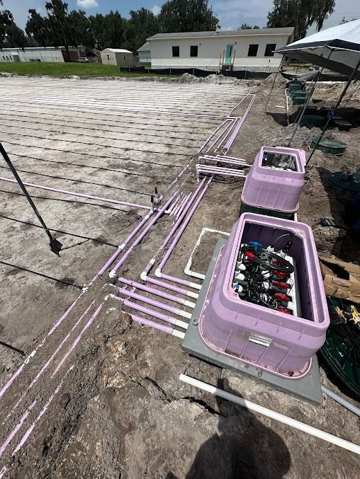 Irrigation system with purple control boxes, white pipes, and a building on a dirt lot.