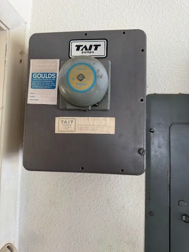 Gray metal box on a wall, with a bell and labels that say 