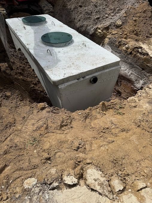Concrete septic tank in an excavated hole, two lid covers visible.