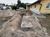 Excavation site with exposed concrete slab near a yellow house; vehicles and trees in the background.