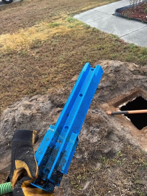 Blue tool held near an open septic tank, set in a yard.