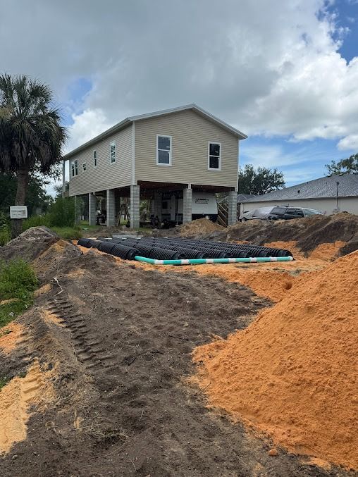 A two-story house on stilts under construction with piles of dirt in the foreground.