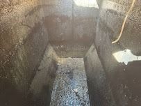 Dark, empty, trapezoidal bin with wet, gray surfaces and a faint light source at the top right.