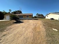 Single-story yellow house with a dirt driveway and a clear blue sky.