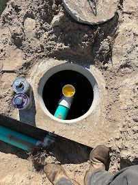 Open septic tank with pipes, a partially-opened lid, and person's boots.