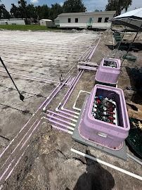 Purple irrigation pipes and valve boxes on bare ground, near a building.