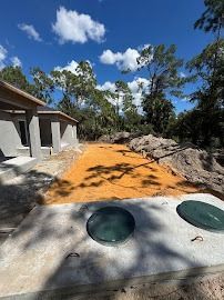Construction site: septic tank with green lids in front of a house, orange sand, and trees under a blue sky.