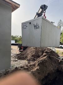 A concrete septic tank suspended by a crane, being placed near a house.