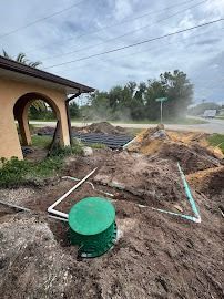 Septic system installation near a house; dirt piles, pipes, and a green lid.