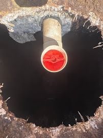 A red valve inside a pipe, surrounded by a dark hole in weathered concrete.