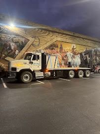 White flatbed truck parked in front of a mural, loaded with what appears to be construction material.