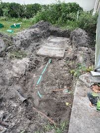Trench with concrete cover, green pipes, and dirt. A construction site near a building.