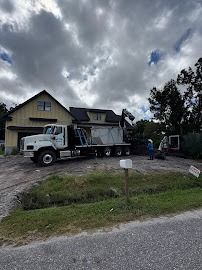 Truck unloading materials at a house, overcast sky. Workers and equipment visible.