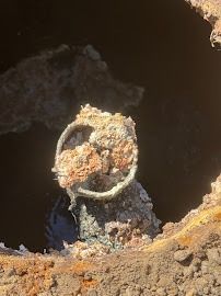 Severely corroded metal pipe in a dark, rusty hole; orange and brown discoloration.