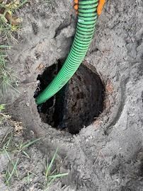 Hole in the ground with a green hose inserted. Earth is surrounding the hole, and grass is visible.