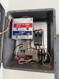 Open electrical box with a level alarm control panel, circuit breakers, and wiring.