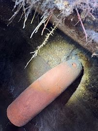 Close-up of a rusty, cylindrical object in a dark, cave-like space, illuminated by a light.