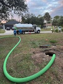 Septic tank pumping service: green hose connected to a tank truck, near a home.