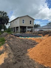 House under construction on stilts, with dirt mounds and buried septic system in the foreground.