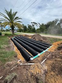 Black septic tanks laid in a rectangular bed, connected by green PVC pipes, on a cloudy day.