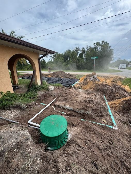 Construction site with septic tank and piping in front of a house under a cloudy sky.