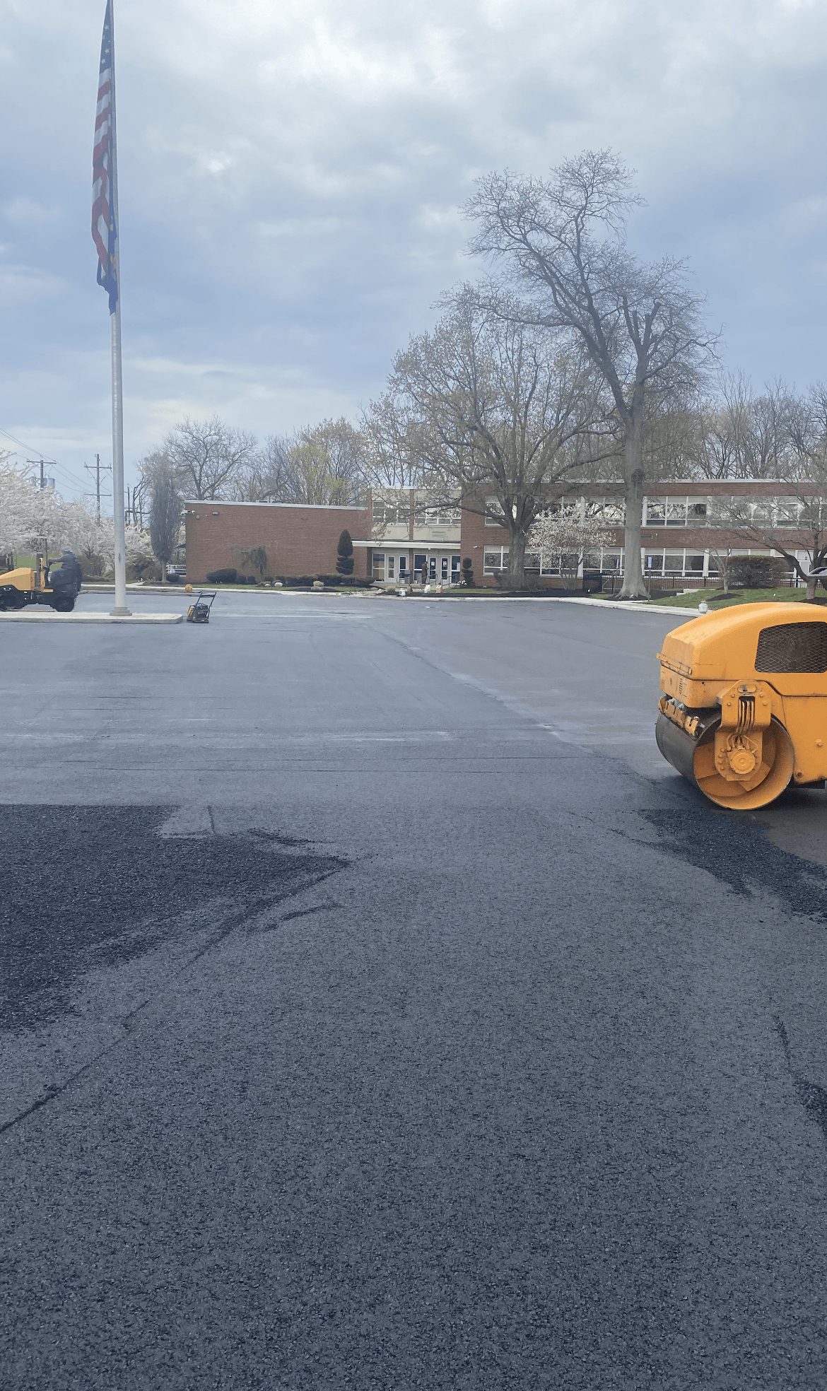 A yellow roller is rolling asphalt in a parking lot
