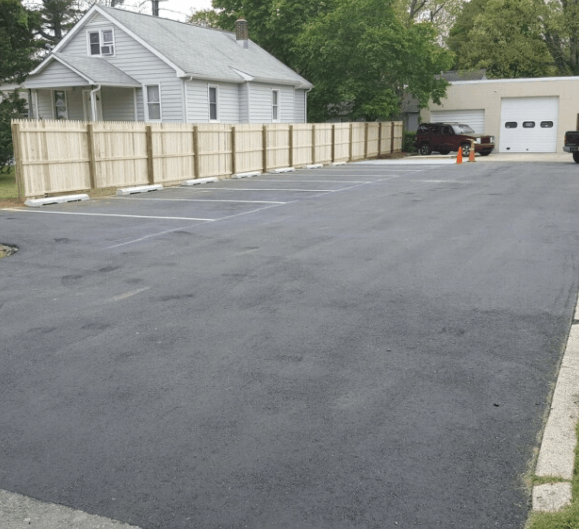 A fenced-in parking lot with a house in the background
