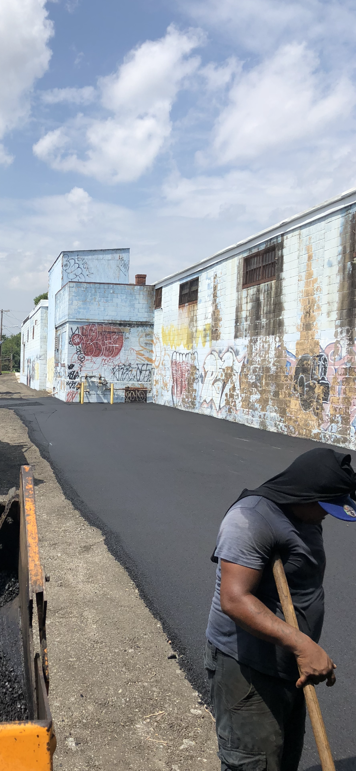 A man is laying asphalt on the side of a road