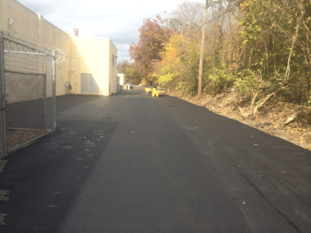 A black road with a fence and trees on the side of it