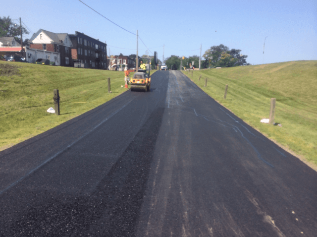 A yellow asphalt roller is driving down a black road