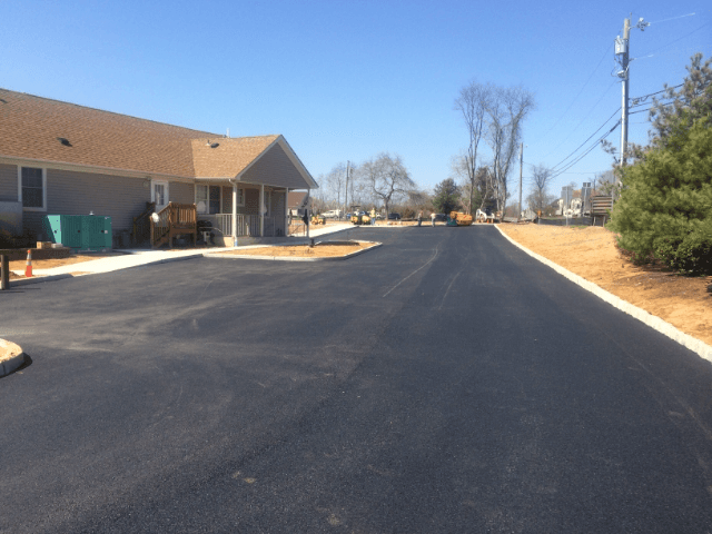 A road with a house in the background and trees on the side