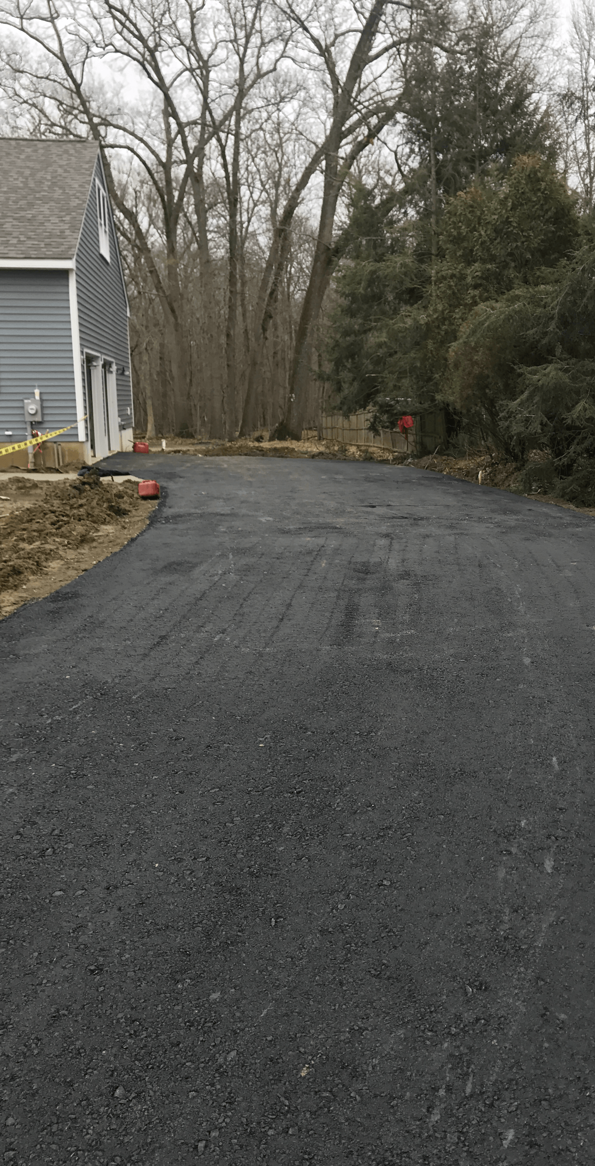A black asphalt driveway leading to a house surrounded by trees