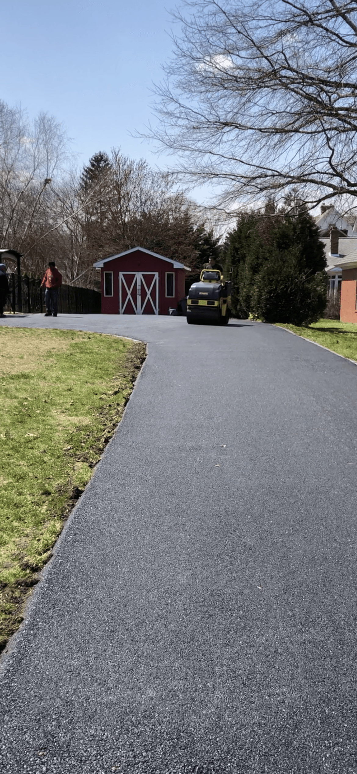 Asphalt roller driving down a driveway next to a red barn