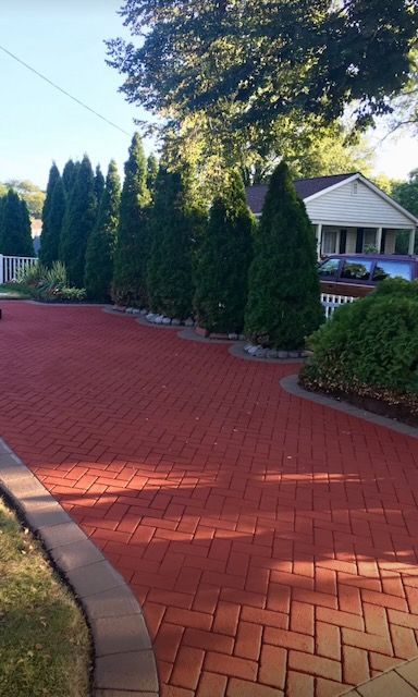 A red brick driveway leading to a house with trees in the background.