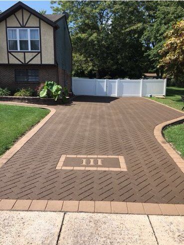 A brick driveway leading to a house with a white fence.