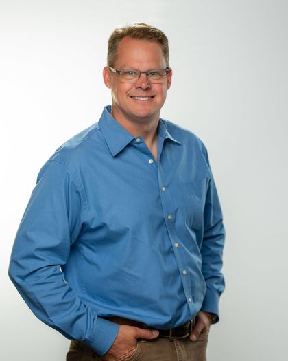 Man wearing glasses and a black uniform, smiling.